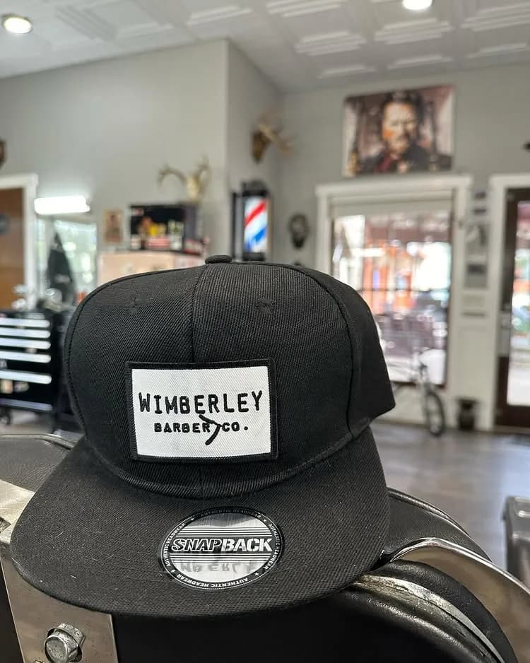Black Wimberley Barber Co. snapback hat resting on a chair