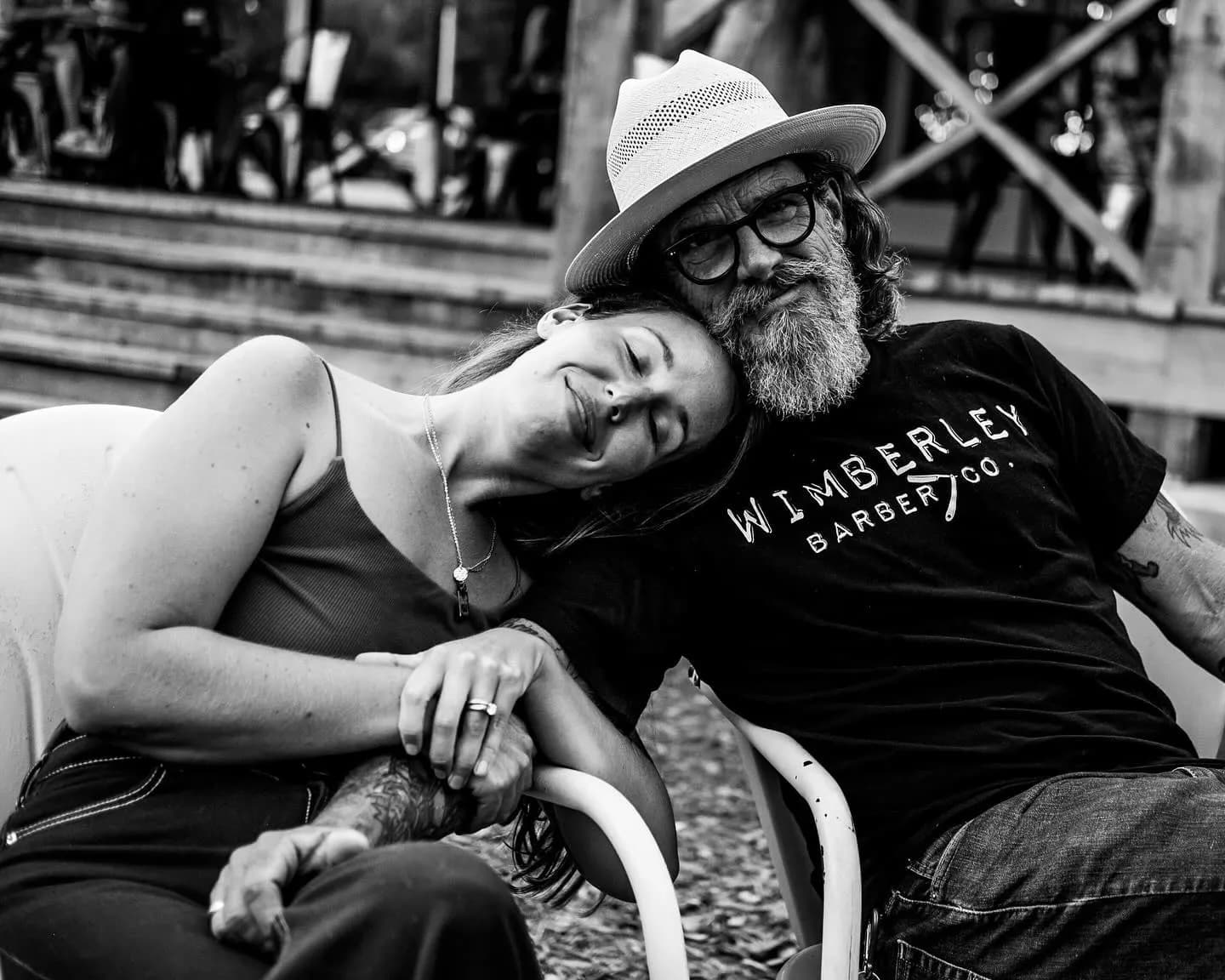 Jake in a Wimberley Barber Co. shirt and straw hat with a woman resting on his shoulder, black and white