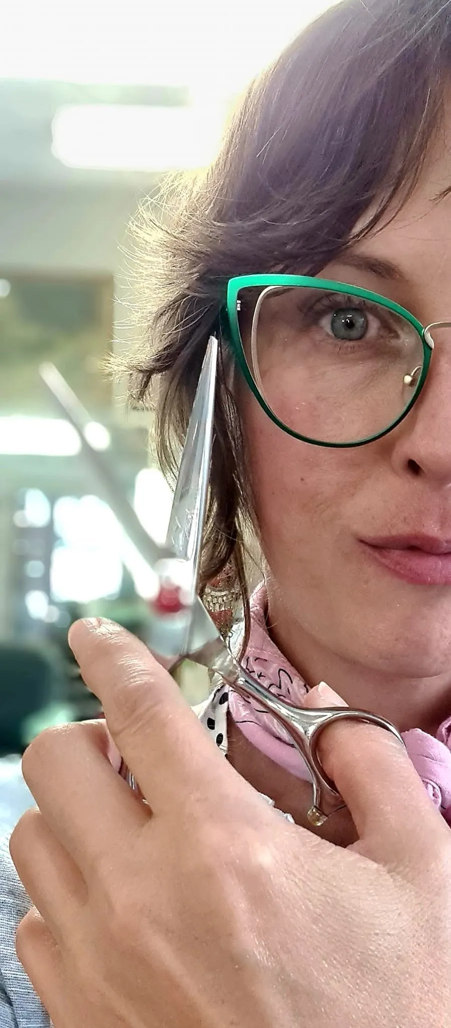 Jill wearing green cat-eye glasses holding scissors close to her face in the salon