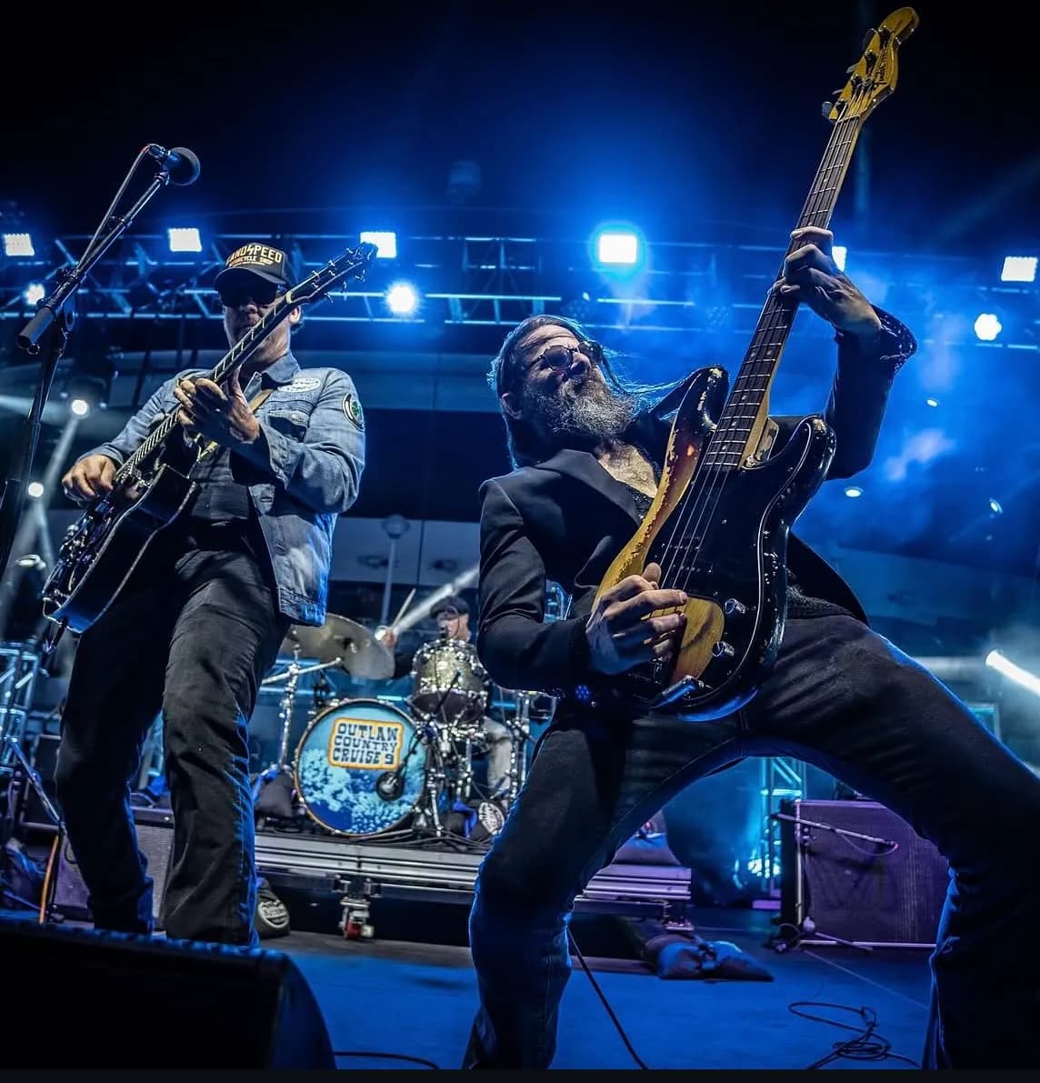 Guitarists performing live on stage with blue lighting at the Outlaw Country Cruise