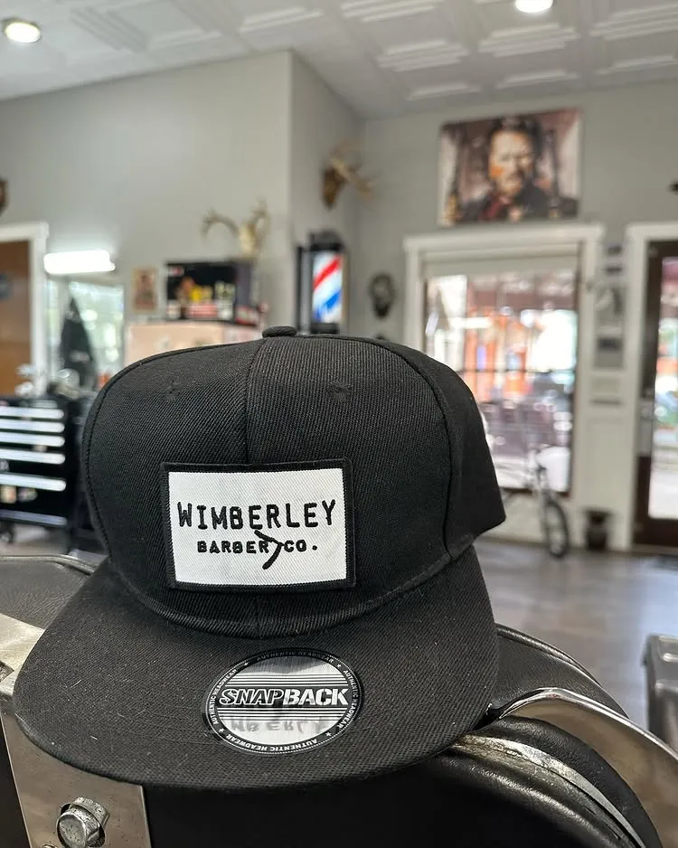 Black Wimberley Barber Co. snapback hat resting on a chair